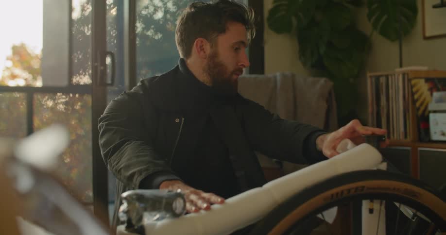 Young bearded man unpacks a bicycle in the living room at home