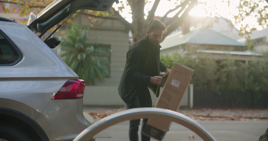 Man unloading a cardboard box from the trunk of his car at sunset