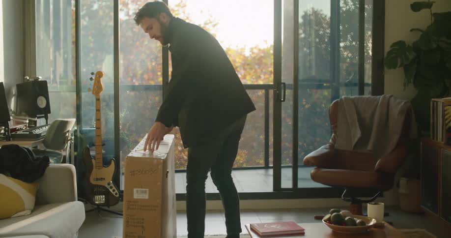 Young bearde man carryng a bicycle packed in a cardboard box into the living room
