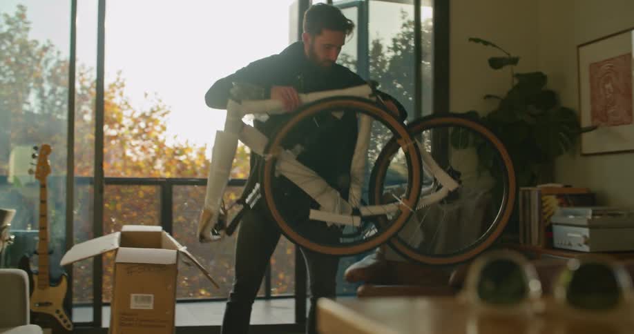 A man in a room taking an unassembled bike from a box with a door in the background