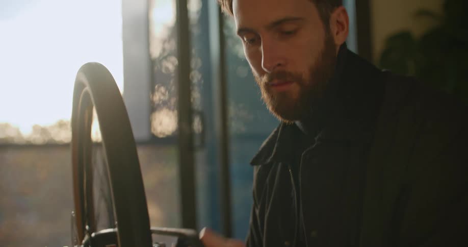 A man spins the pedal of a bike checking the wheel of it inside a building