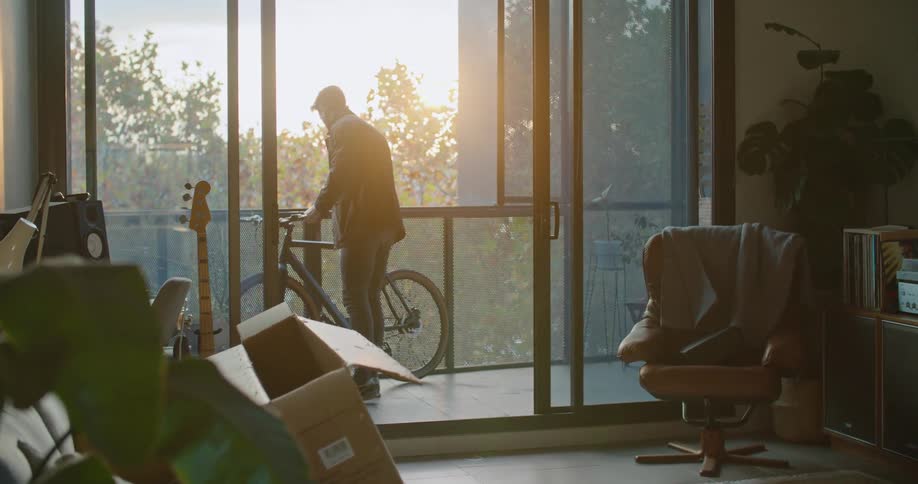 A man is putting his bicycle out on the balcony