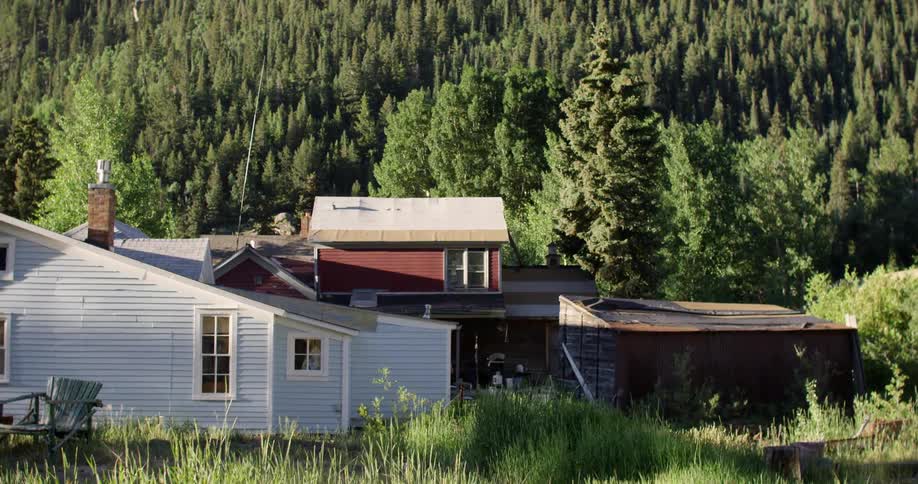 A house sits by the bottom of a hill covered with trees