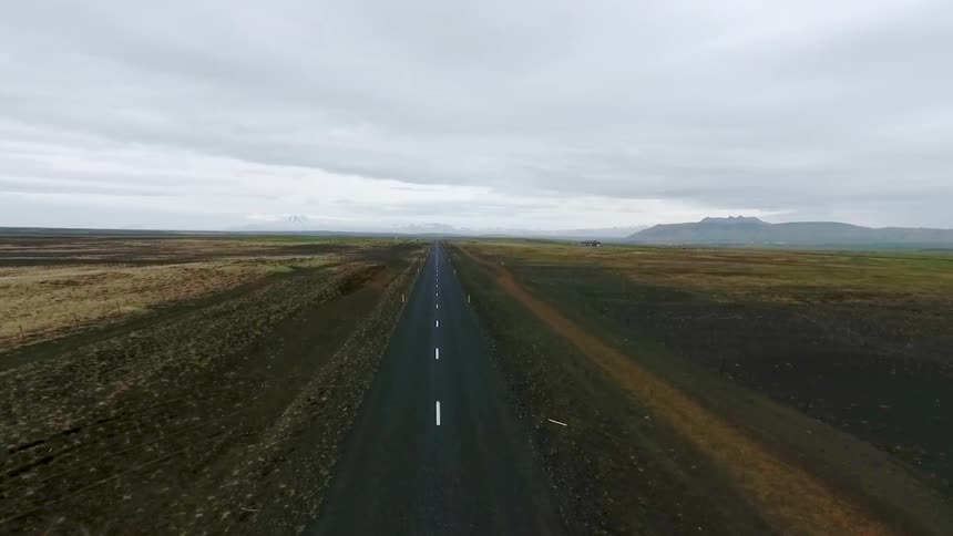 Moving down a small road with large green fields on either side