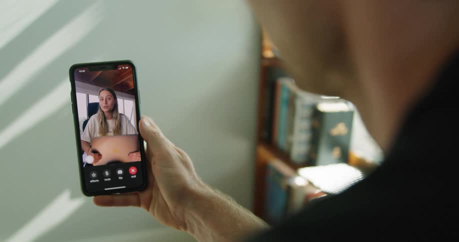 A man sits in a room beside a bookshelf on a video call with a woman holding a laptop