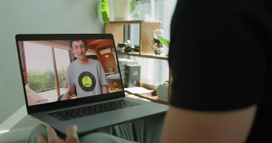 A man holds a laptop on his knee as he talks to a teenager on it and they give each other the peace sign