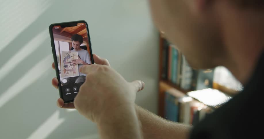 A teenage boys shows his dad artwork as they video chat on a cell phone