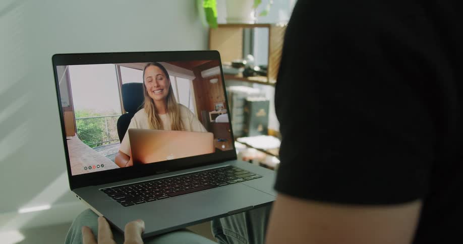 Man holding a laptop where a woman is talking on a video call from another location