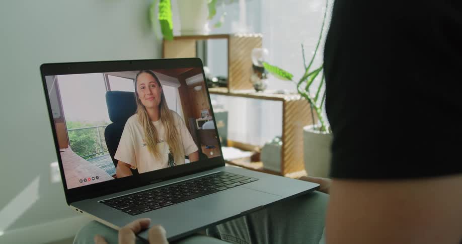 Man with a black shirt sits down and makes a video call with a blonde woman on laptop