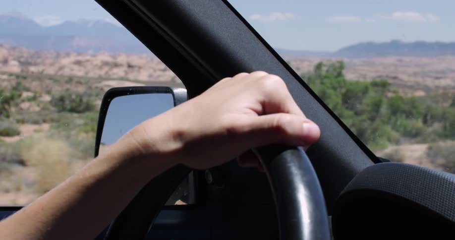 Close up of a hand steering a car as it drives