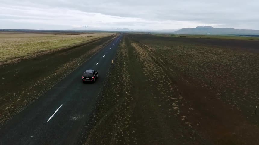 A vehicle traveling down a road between two grassy fields during the day