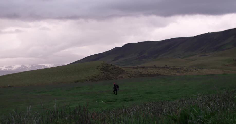 Person walking across a grassy field on a cloudy day