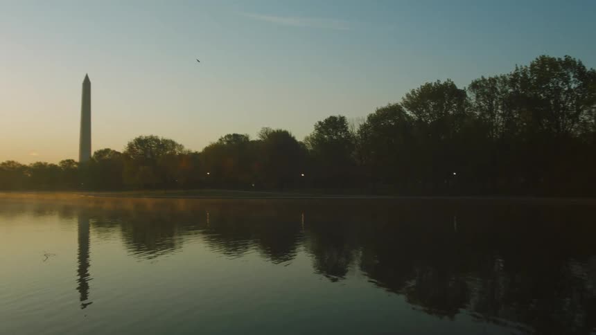 Rippling water reflects surrounding trees and nearby washington monument under red tinted sky