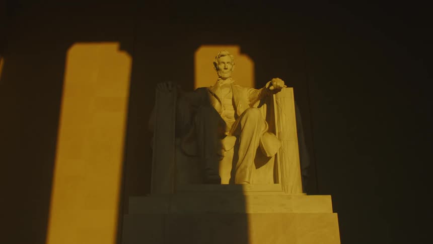 A large sculpture of a seated abraham lincoln is illuminated by sunlight at the lincoln monument