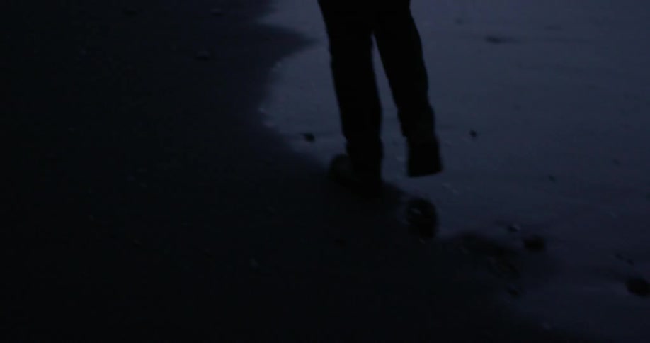 A man walks on a beach near the water at night