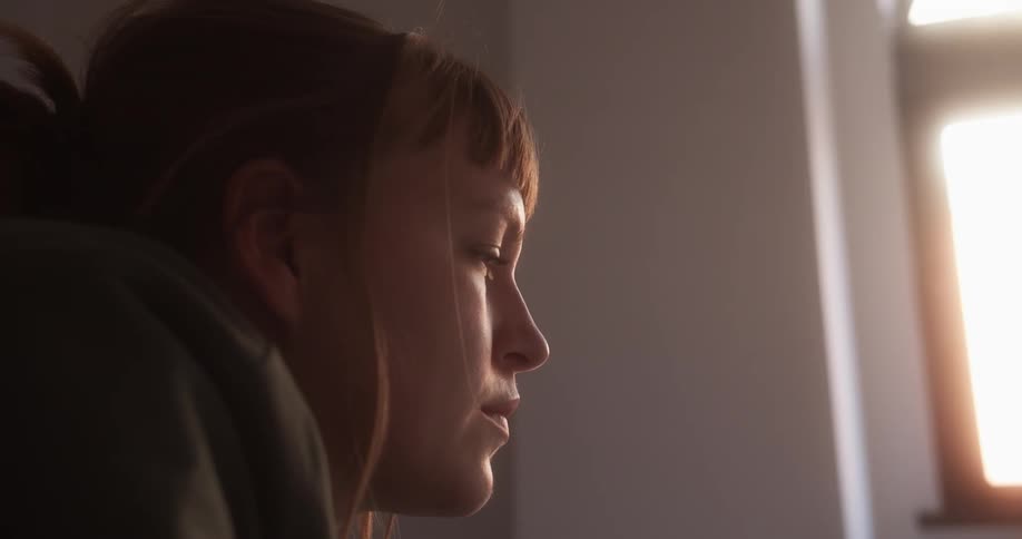A woman in a room smiling with a wall and window in the background