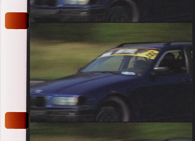 Multiple cars drift on a curve during a race as crowd watches