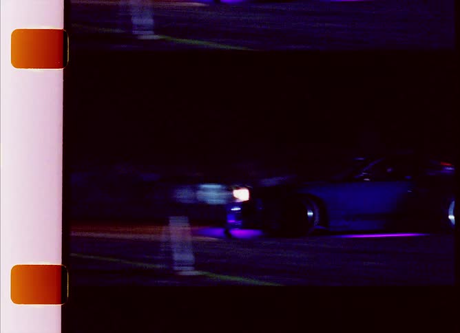 Sports car drifting on a track at night caught on vintage film