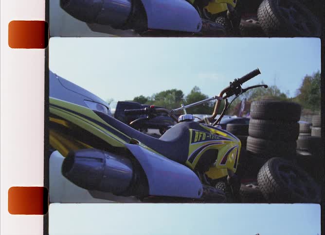 A brightly painted dirt bike sits in an open lot filled with stack of tires
