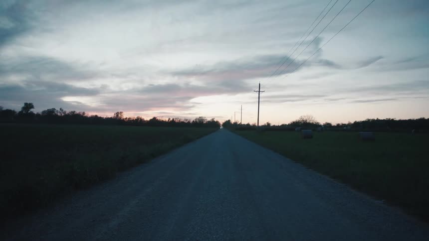 A road next to farmland with bales of hay on the field
