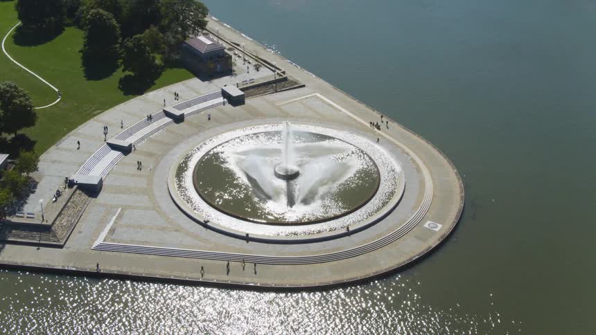 A large water fountain serves as a monument that is located along a river near a large city