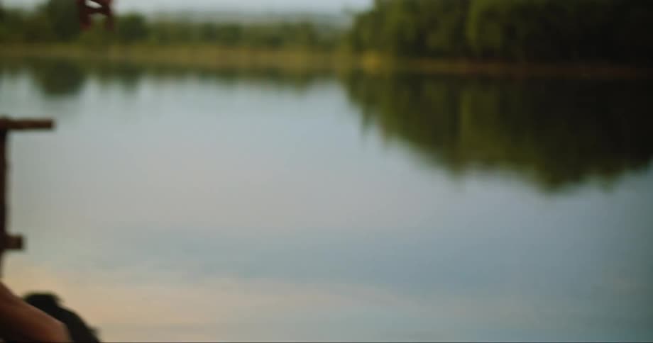 A male and female stand next to a lake and the male skips a pebble to the water