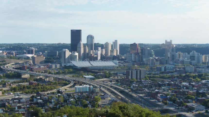 The skyscrapers of a metropolis loom over a long overpass during the day