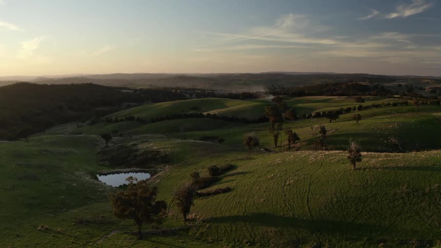 A landscape with trees hills and a pond with the sky and clouds in the background