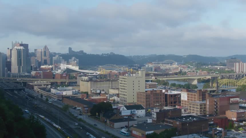 Traffic moves across bridges over river and through streets of city bordered by mountains on misty day