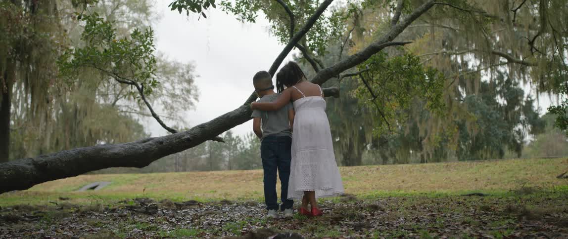 Siblings hugging in front of a fallen branch in a park at daytime