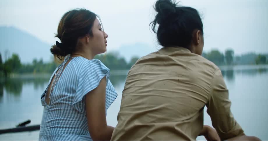 A young couple sit together next to a large lake and enjoy their surroundings together