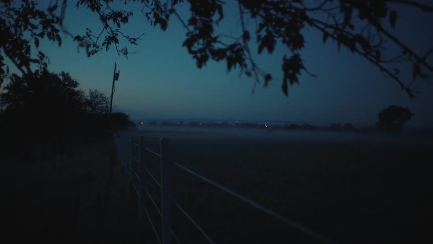 A landscape view of a grassland with lights in the far distance