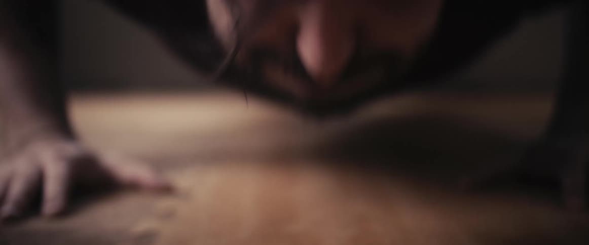 A sweaty man strains and trembles slightly as he performs a series of push ups
