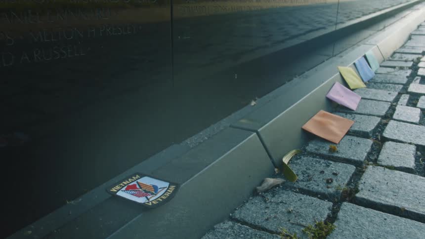 Polished black stone of vietnam memorial reflects trees as colored envelopes sit on ground near memorial base