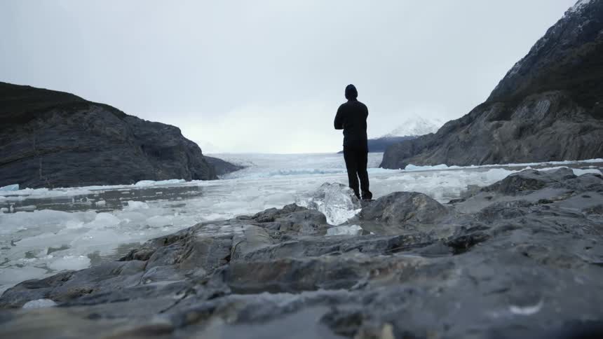 Man wearing a black wet suit standing on the frozen coast in the mountains