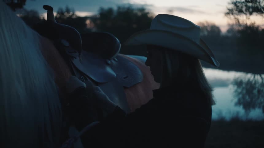 A woman securing a saddle to a horse