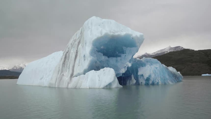 An iceberg in the water and snow covered mountains in the distance