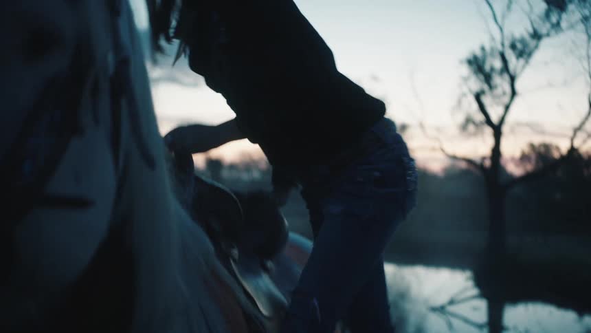 A woman in a cowboy hat gets a foothold in the saddle stirrup as she mounts her horse
