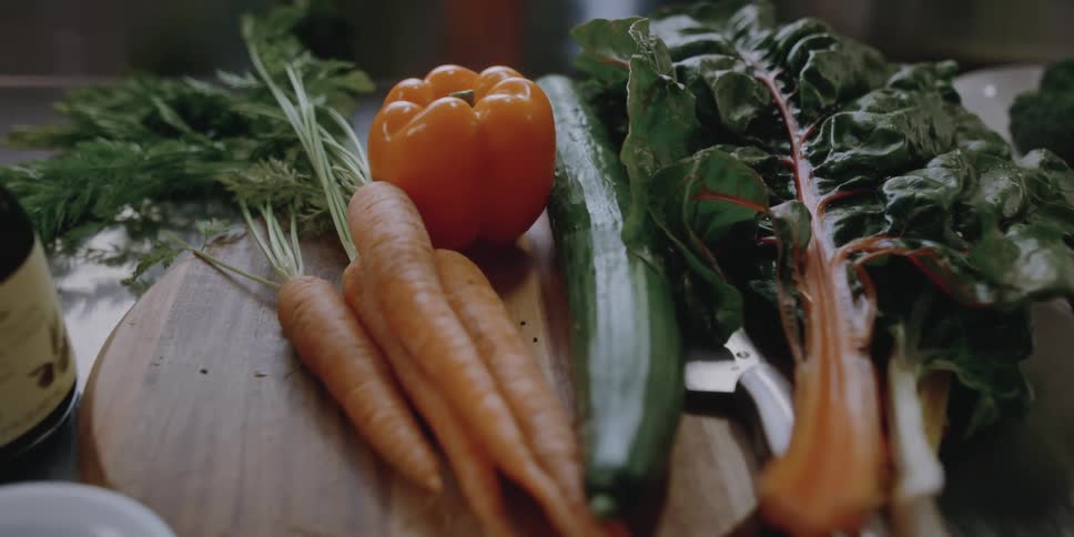 Various vegetables partially cover knife on wooden chopping board