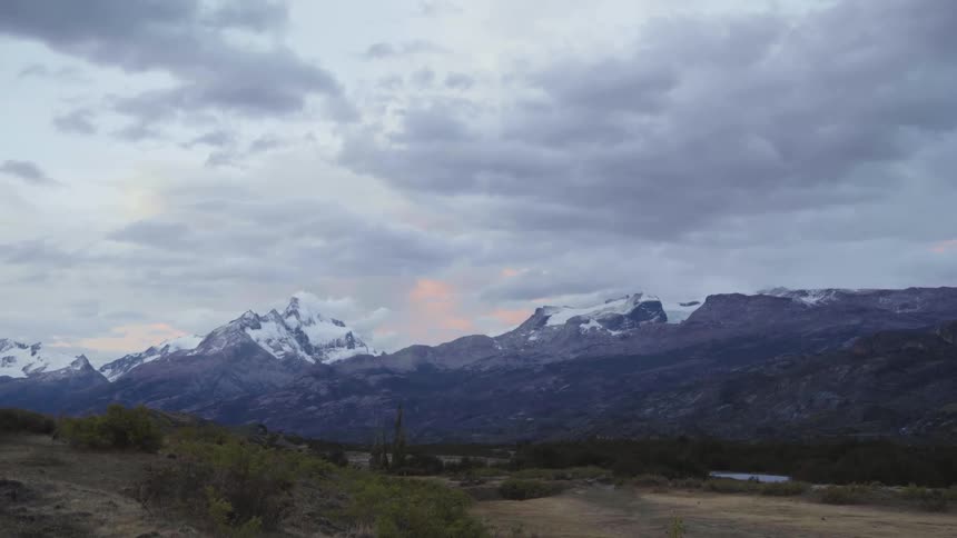 Snow capped mountains border scrubby plains under cloudy sky