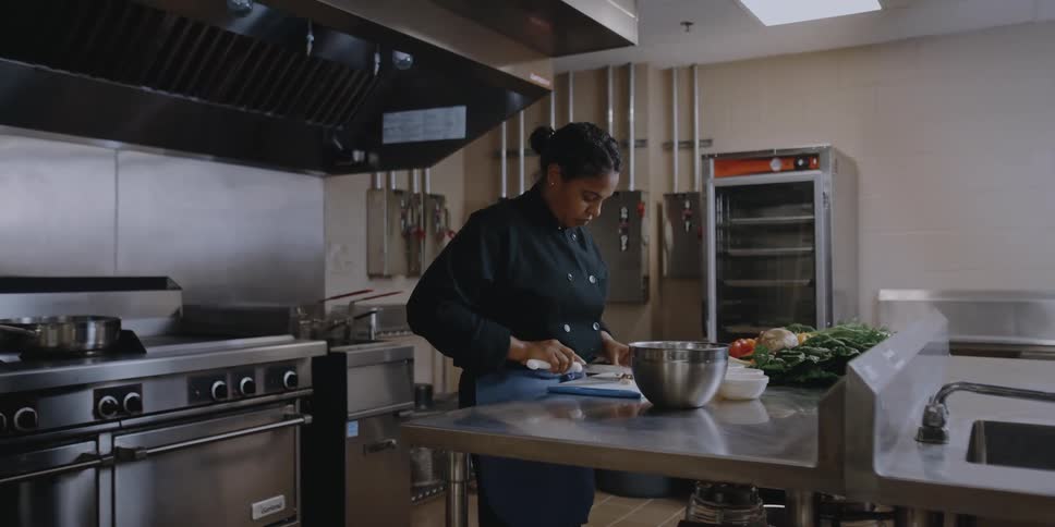 A chef slices food on a cutting board in a stainless steel professional kitchen