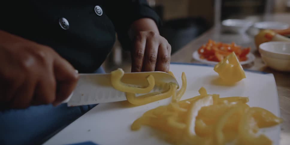 A person uses a knife to slide yellow peppers in a restaurant kitchen