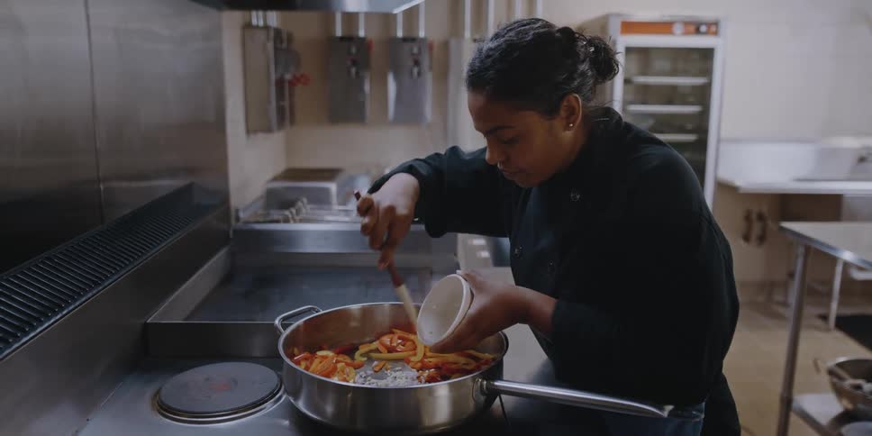 A chef scrapes an ingredient into a large pan in a professional kitchen