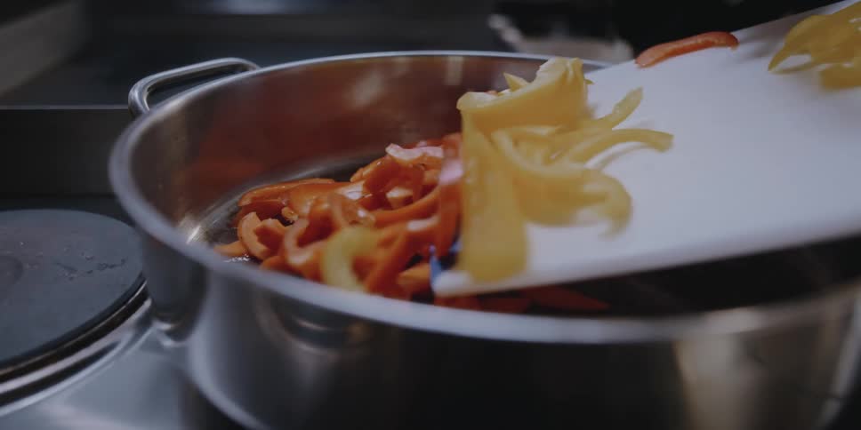 A person in a kitchen putting vegetables in a pot from a cutting board