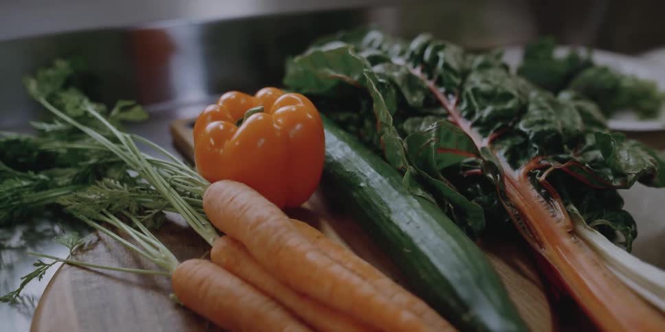 Vegetables lie atop a wooden cutting board on a steel surface in an industrial kitchen