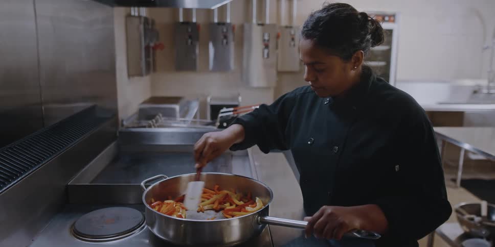 A woman is weariing a chef uniform and making a dish on the stove