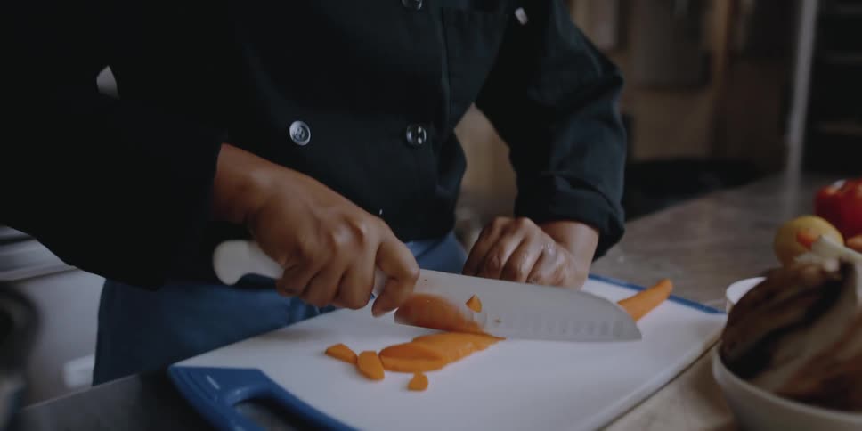 A chef slices a carrot on a plastic cutting board in an industrial kitchen