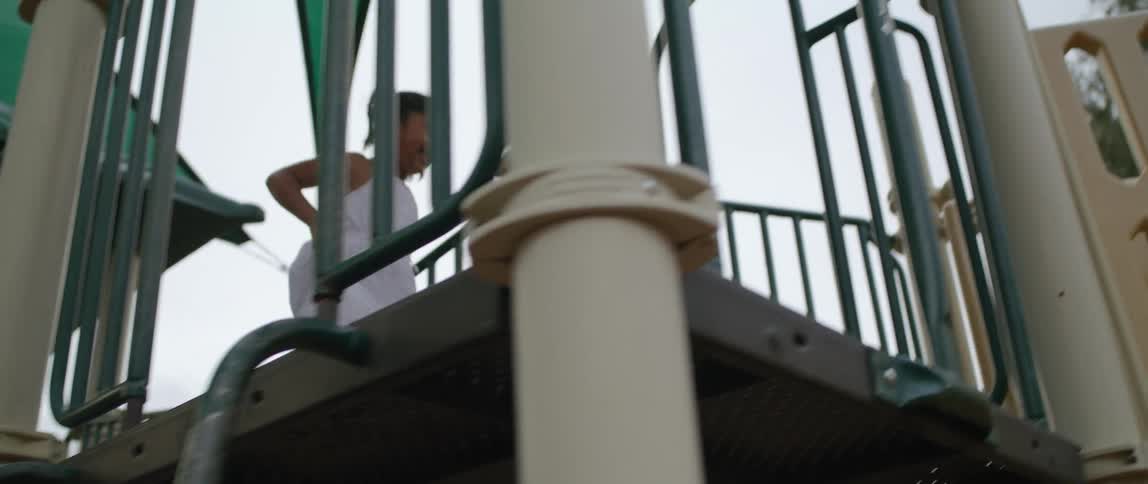 A young girl in a white dress happily smiles as she runs atop a play structure at a playground