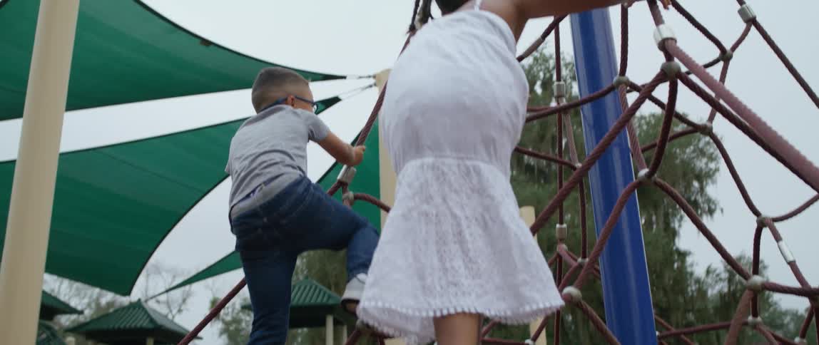 A young boy and girl both excitedly climb a series of ropes on a play structure at a park