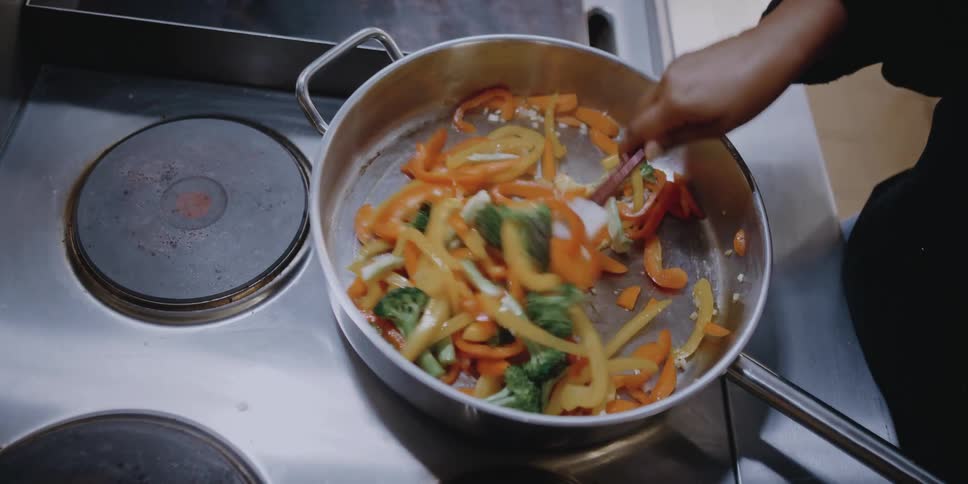 Woman stirs vegetables in skillet on stove top